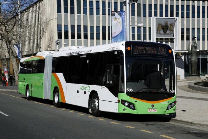 Green-and-white city bus driving past a modern building on a street