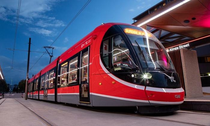 Red modern tram at a station platform at dusk, with illuminated front lights and sleek windows