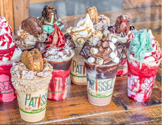 Assorted colorful milkshakes topped with whipped cream and candy on a wooden table