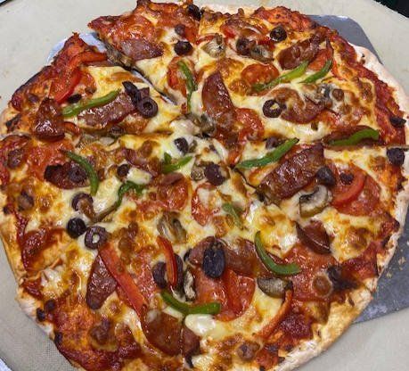 A vegetable and meat pizza on a gray surface, topped with olives, peppers, and melted cheese