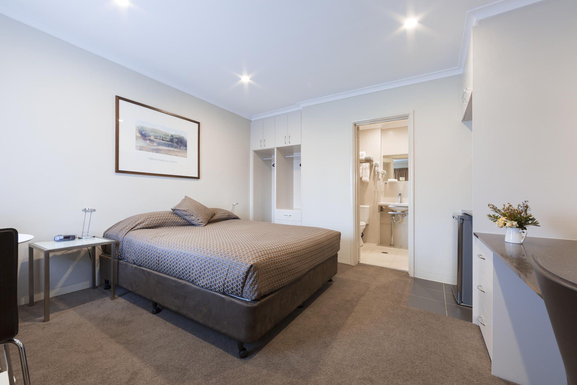 Modern bedroom with a bed, nightstand, framed art, and an open doorway to a bathroom