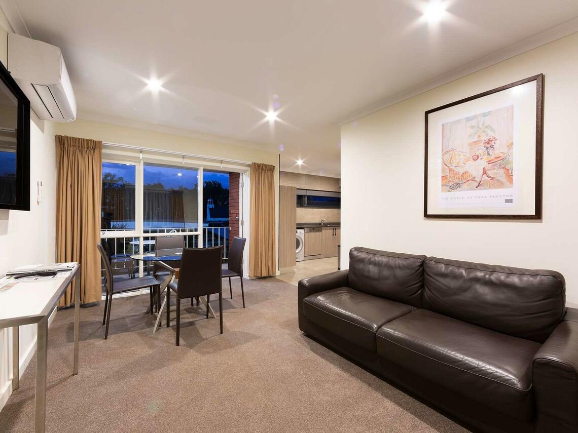Modern living room with dark sofa, dining table, and sliding glass doors to a balcony.
