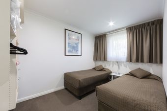 Small bedroom with two single beds, white walls, framed art, and a window with curtains.