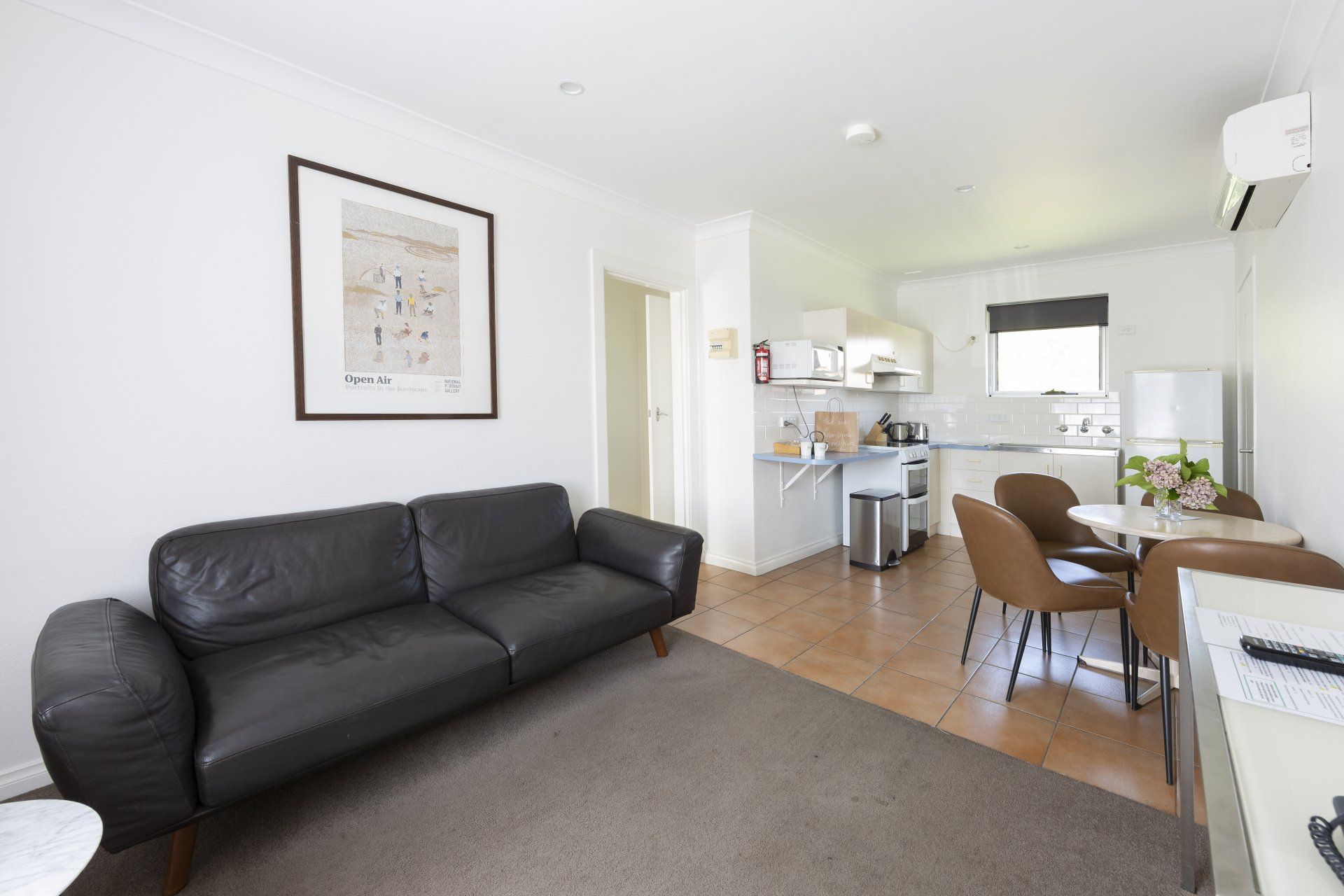 Bright living room with black sofa, dining table, and open kitchen in the background