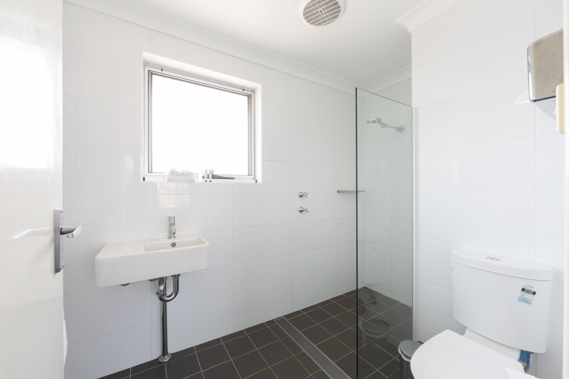 Modern white bathroom with sink, toilet, frosted shower enclosure, and dark tile floor