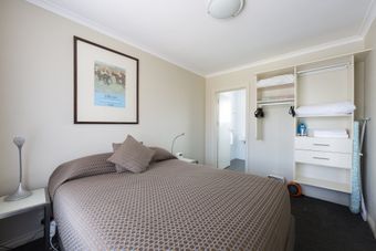 Small beige bedroom with a bed, framed art, and an open closet organizer.