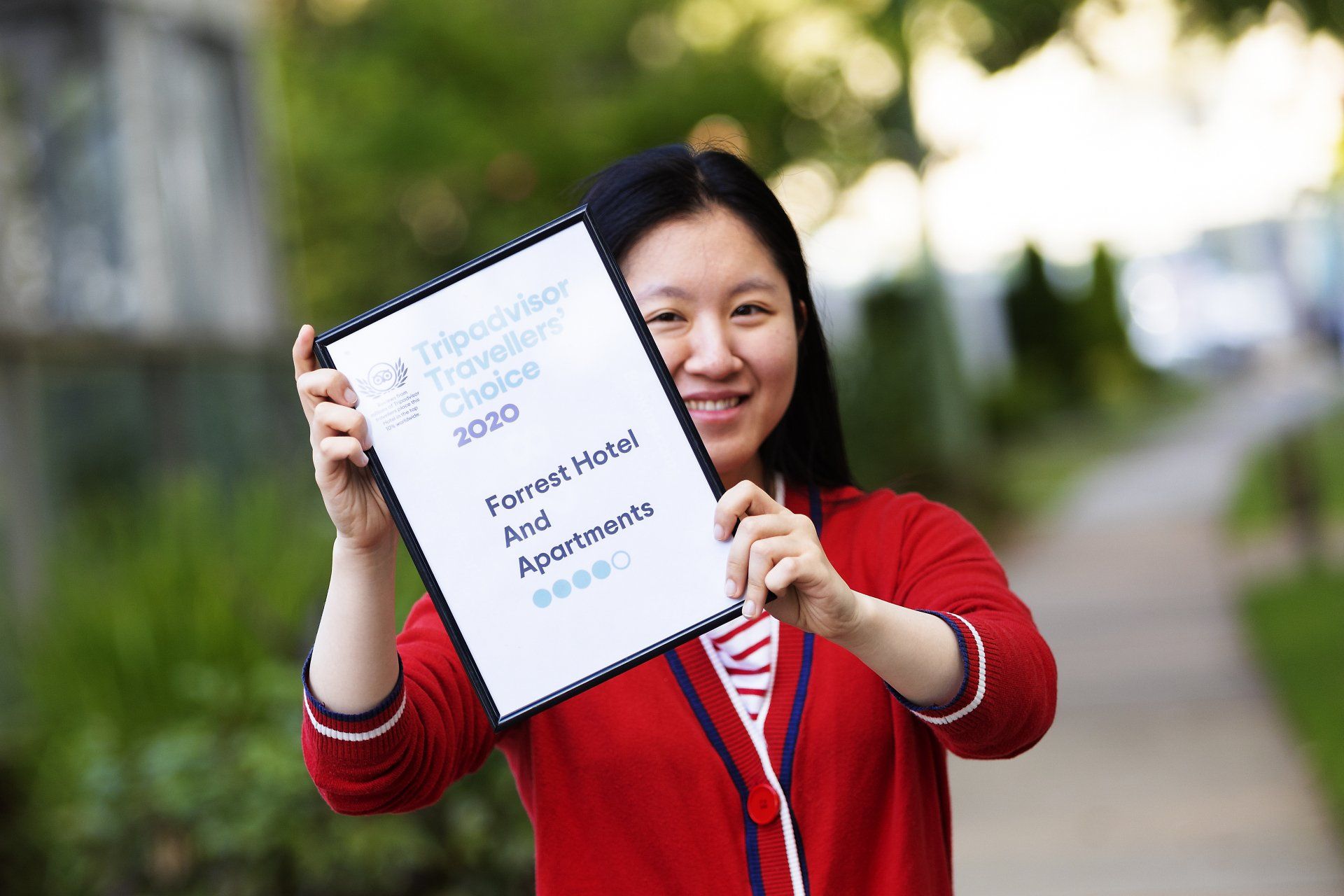 Woman in red sweater holding a framed sign outdoors and smiling at the camera