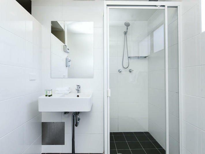 Bright white bathroom with sink, mirror, and a walk-in shower with black tile floor.