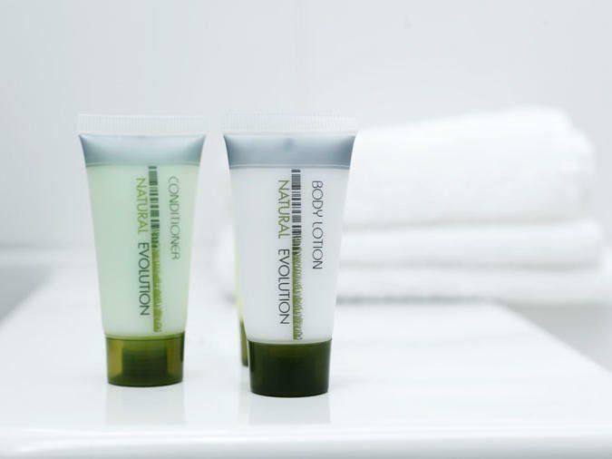 Two skincare tubes on a white shelf beside folded white towels