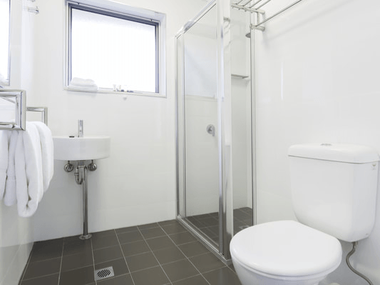 Bright white bathroom with toilet, sink, shower, and window, featuring dark tile flooring.