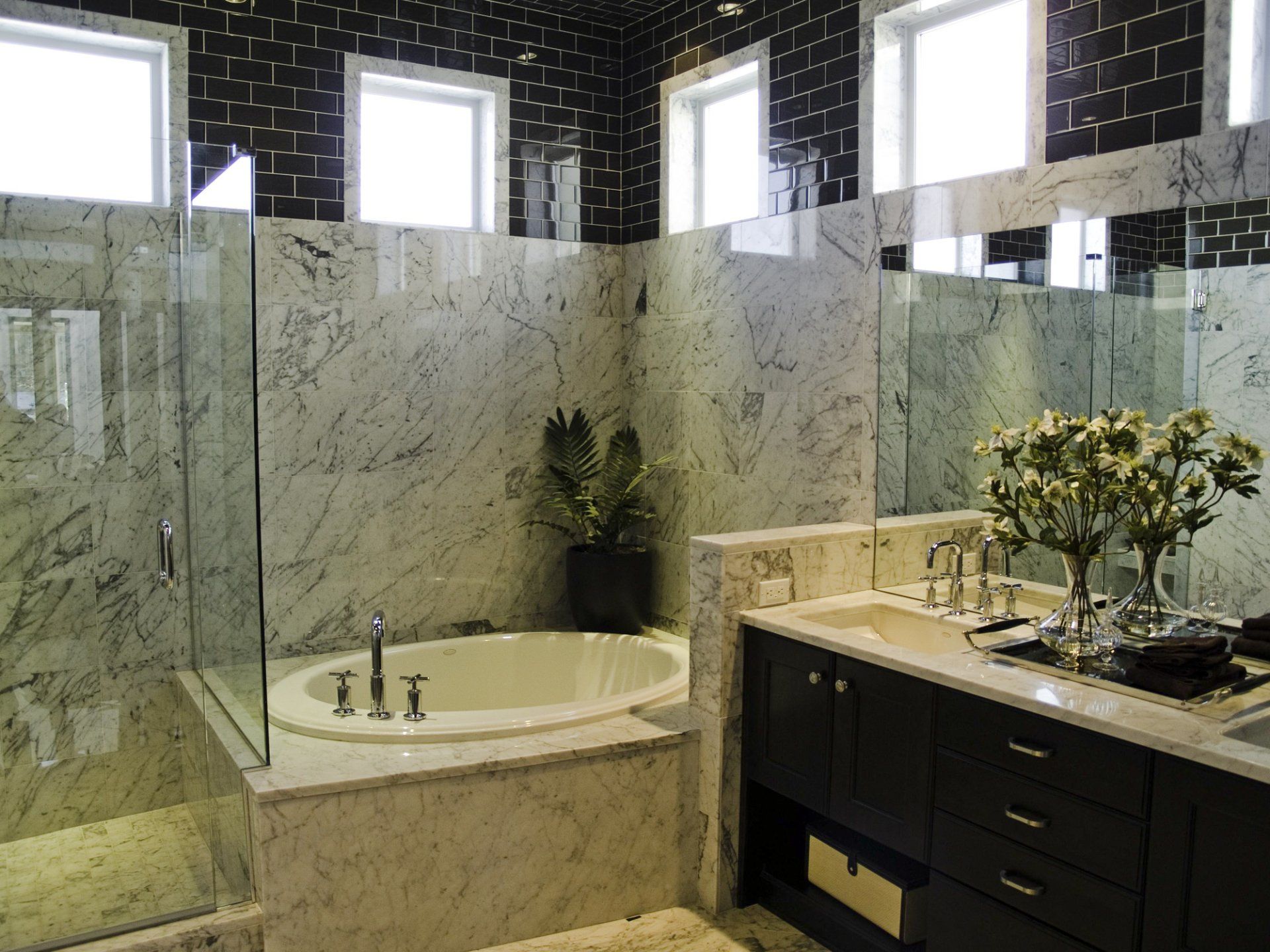 Elegant bathroom with marble walls and black tile accents, featuring a tub, shower, and dark wood vanity.