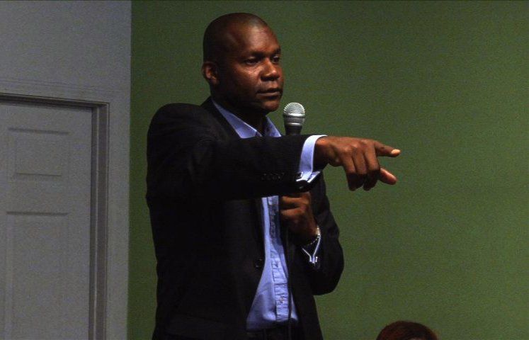 A man in a suit is pointing at something while speaking into a microphone
