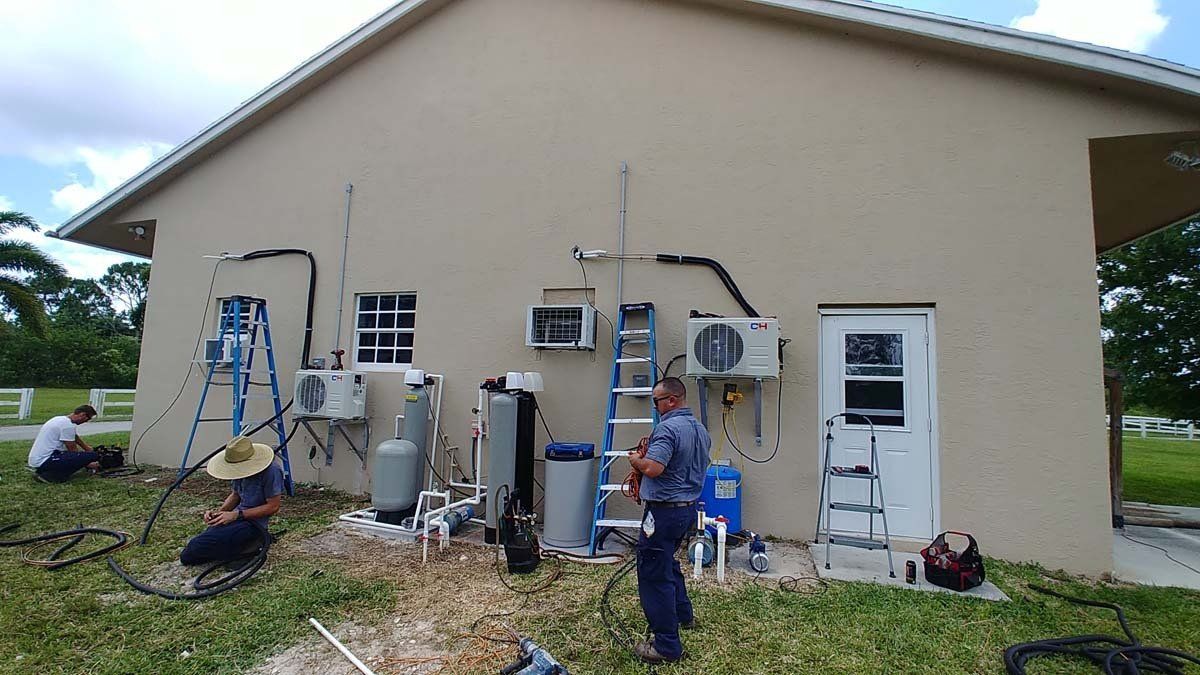 Technicians working on outdoor HVAC and utility equipment beside a beige building
