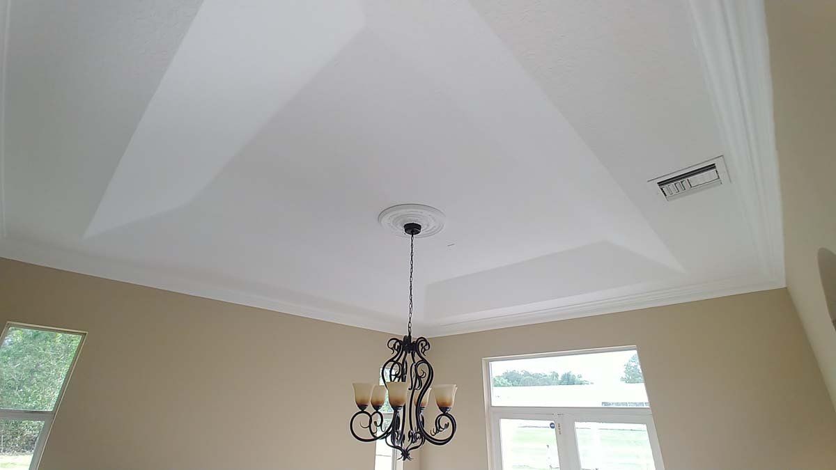 Beige room with a tray ceiling, central chandelier, and windows letting in daylight