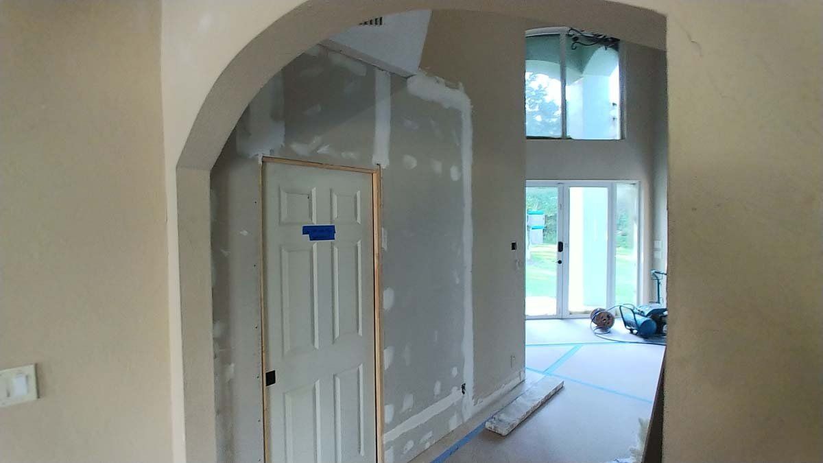 Interior hallway under renovation with arched doorway, white doors, and bright windows at the far end