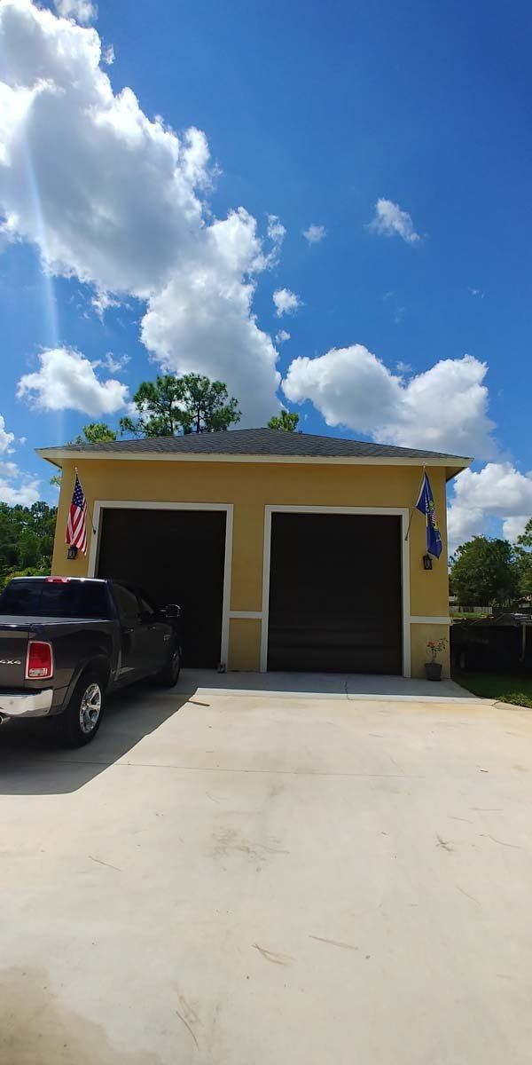 Yellow garage with two open bays, a black truck parked in front, under a blue sky with clouds.