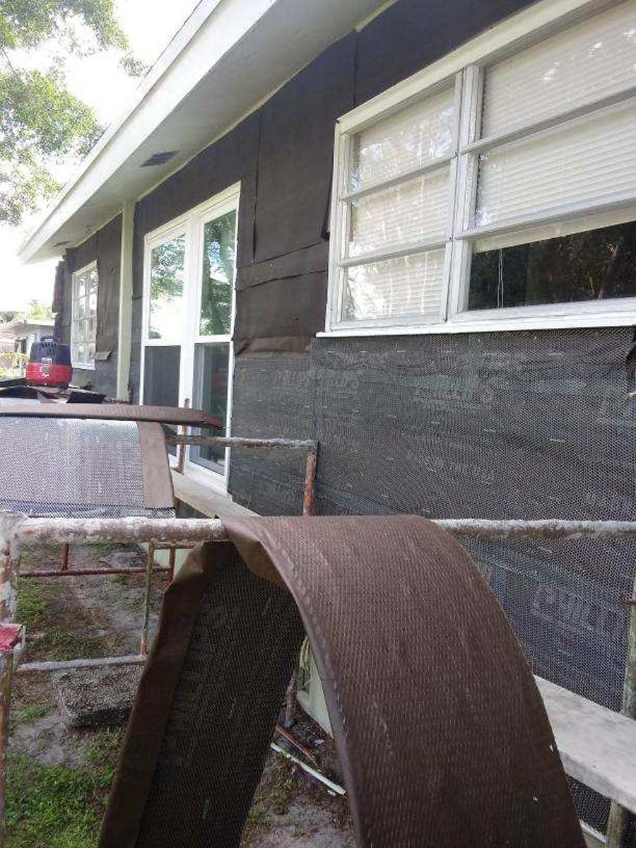Damaged porch railing and bent metal chair beside a house with white windows and dark siding