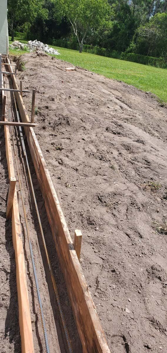 Freshly dug dirt trench along a concrete edge beside a grassy area and trees