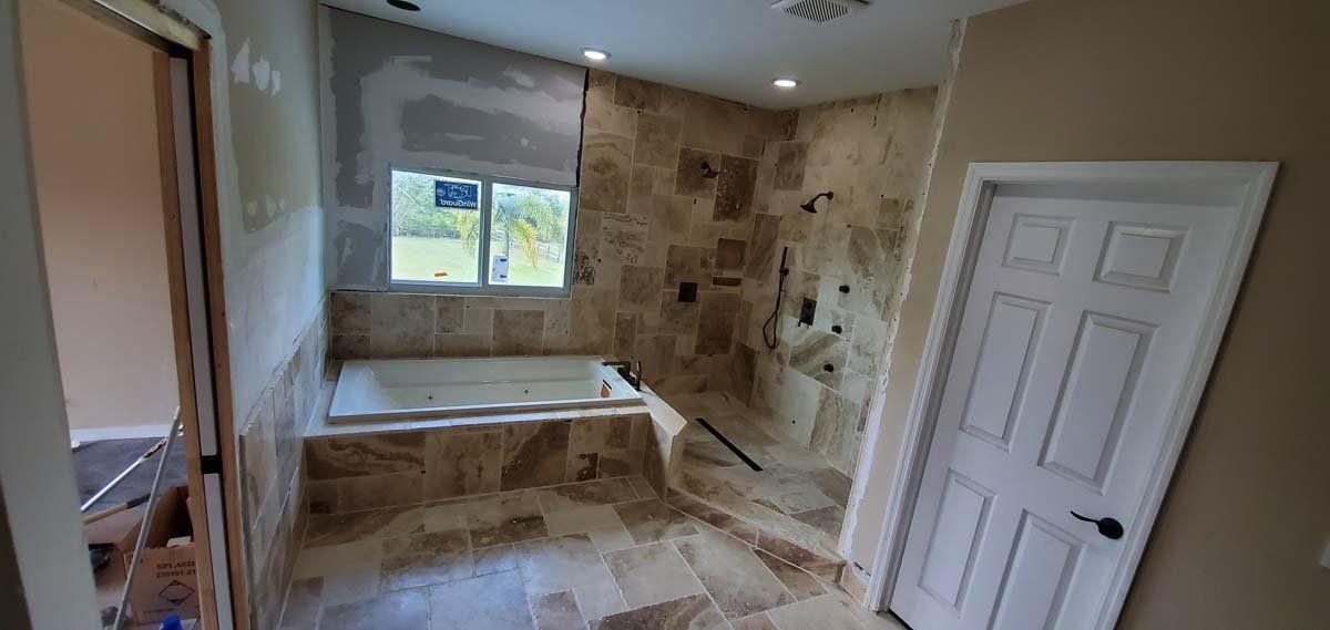 Bathroom with a built-in tub, tiled walls and floor, window, and white door