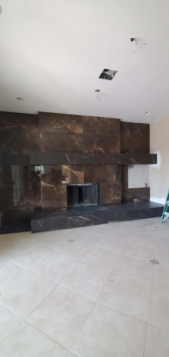 Empty living room with beige tile floor and a dark stone fireplace on the back wall.