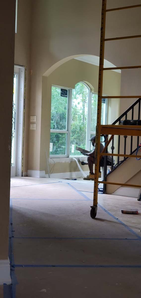 Partially renovated room with ladder, arched window, and construction materials near a staircase