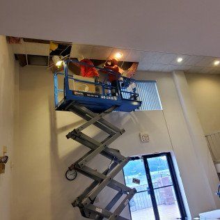 Scissor lift with workers at a ceiling opening inside a building lobby