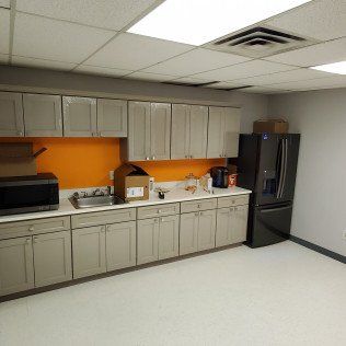 Break room with beige cabinets, orange backsplash, sink, microwave, and black refrigerator
