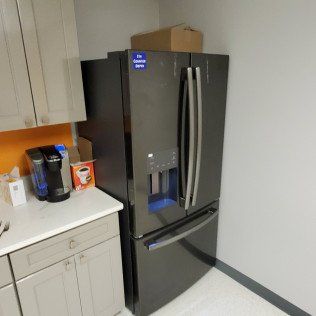 Modern kitchen with a black French-door refrigerator beside white cabinets and a countertop coffee maker
