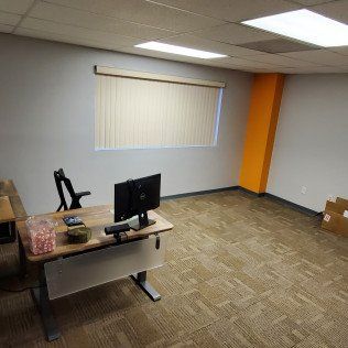 Empty office with desk, computer monitor, window blinds, and an orange accent wall