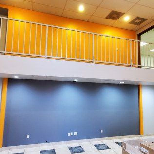 Empty modern room with blue walls, orange upper level, and white railing under bright ceiling lights
