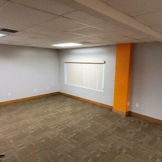 Empty office room with gray walls, brown carpet, drop ceiling, and an orange accent column.