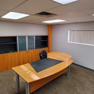 Empty office with a wooden desk, black chair, cabinets, and window blinds.