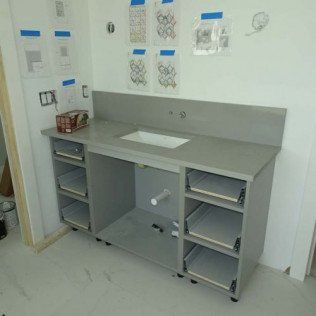 Gray exam room desk with cabinets, wall-mounted charts, and a sink on the left.