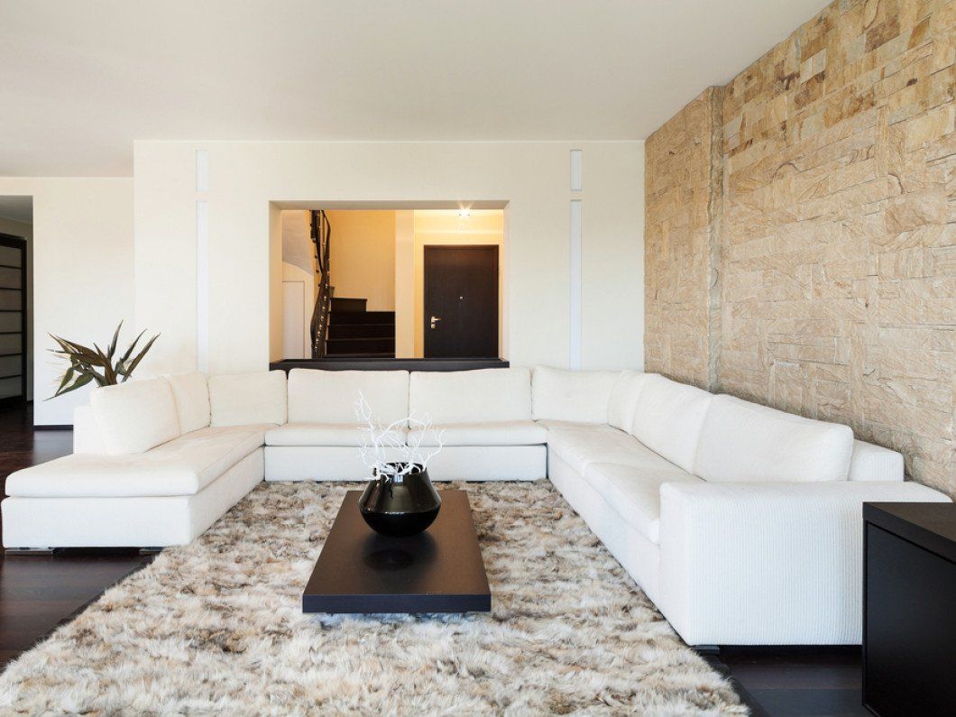 Modern living room with white sectional sofa, shag rug, dark coffee table, and stone accent wall