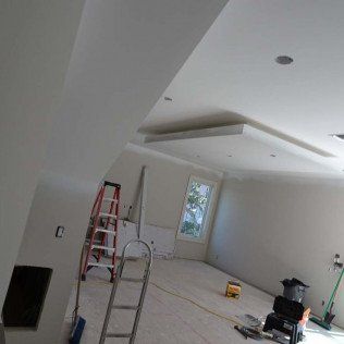 Renovation in progress in a white room with ladders, tools, and a partially finished ceiling.