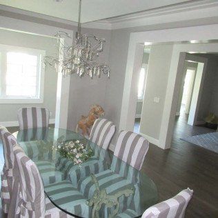 Dining room with glass table, striped chairs, chandelier, and a teddy bear near the window.