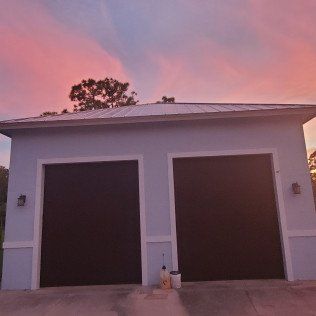 White two-car garage at sunset with pink sky and a bucket by the door