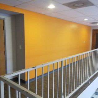 Interior hallway with a bright yellow wall, gray doors, and a white railing