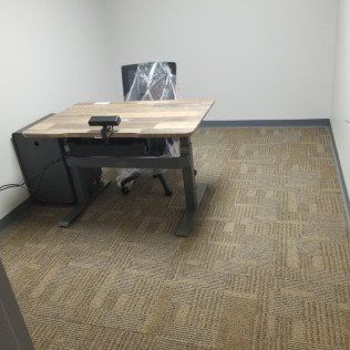 Empty office cubicle with a desk, chair, and beige carpet tiles.