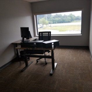 Empty office with a standing desk and computer beside a large window overlooking greenery