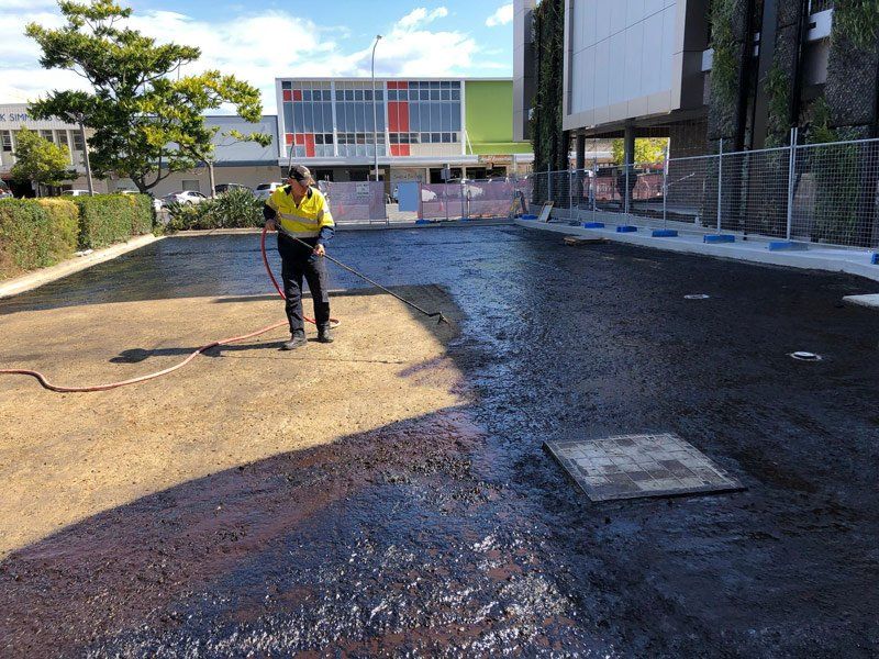 A man is spraying asphalt in a parking lot with a hose.