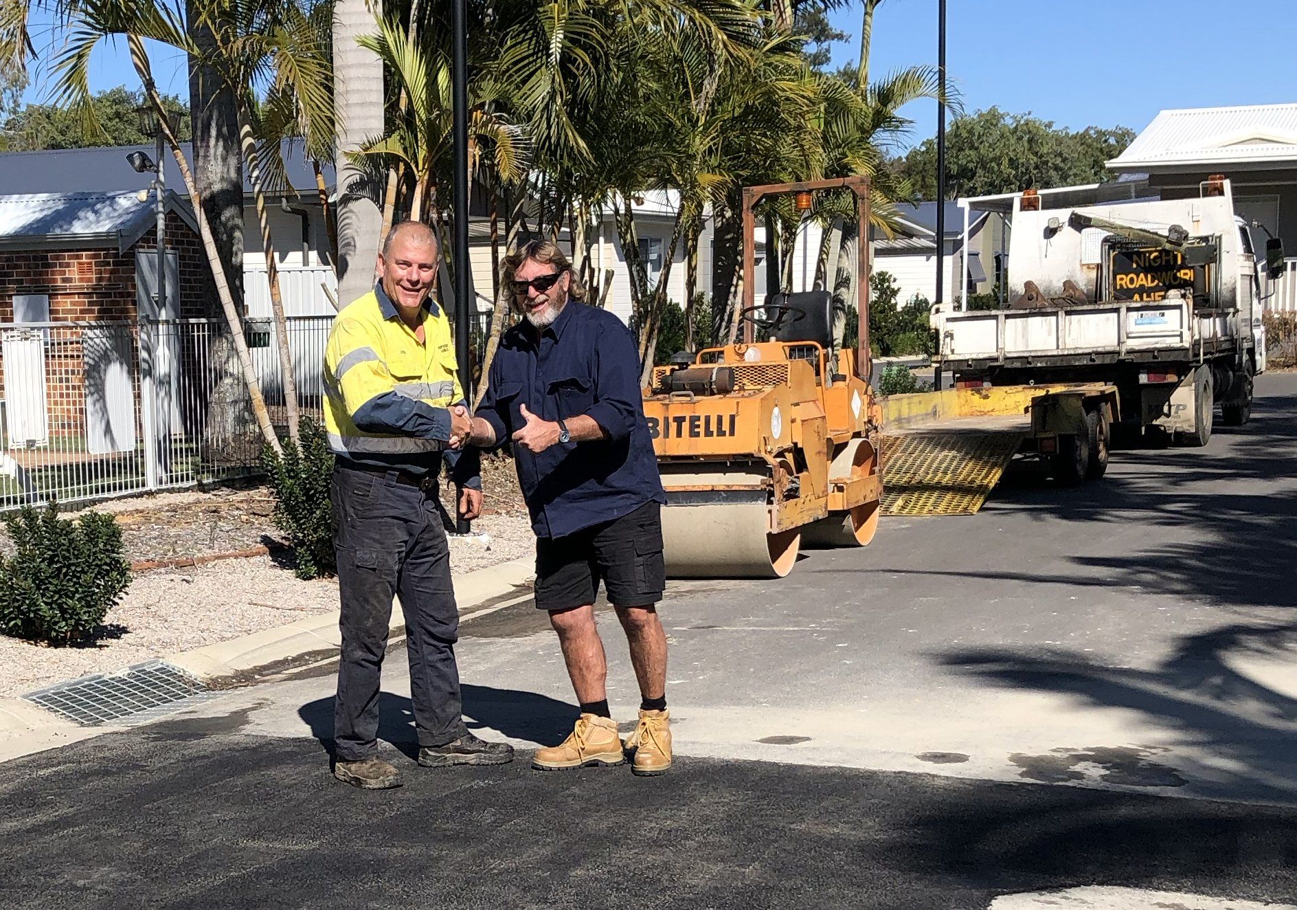 Two men are standing next to each other on the side of a road.