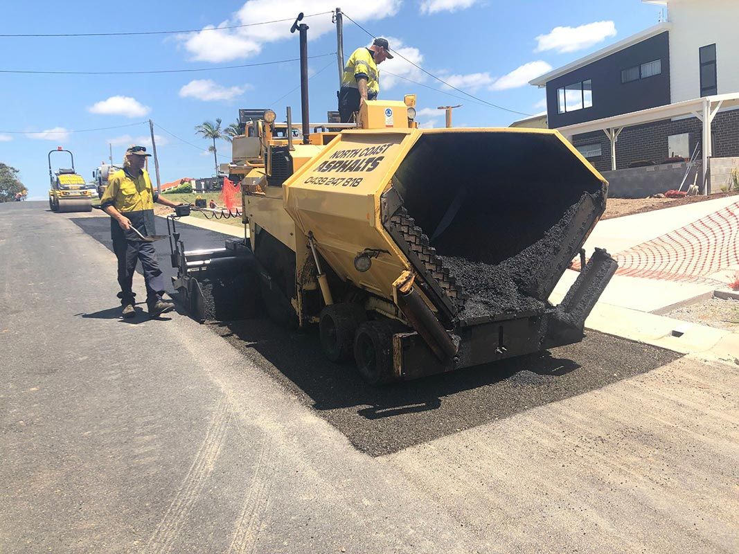 A man is standing next to a machine that is laying asphalt on a road.