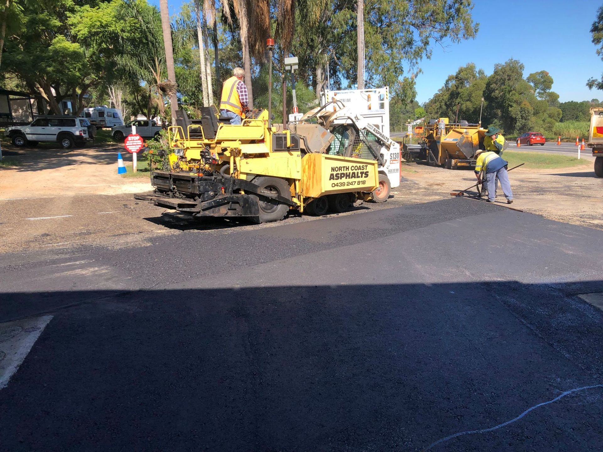 A yellow truck is being used to spread asphalt on a road.