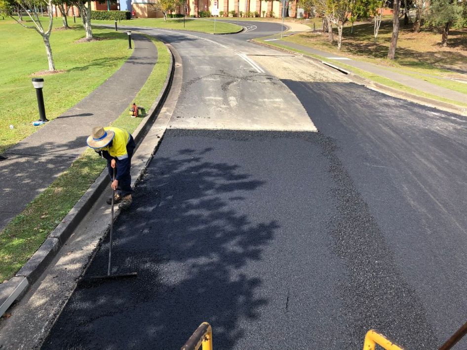 A man is laying asphalt on the side of a road.