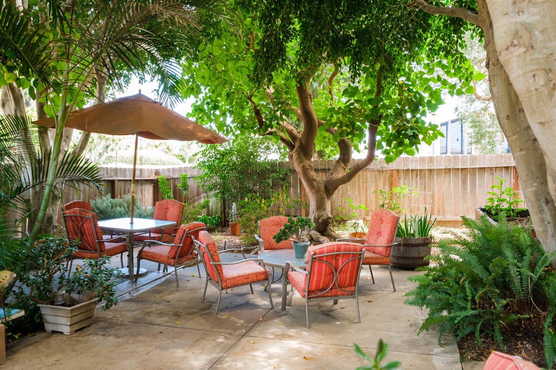 A patio with a table , chairs and umbrella under a tree.