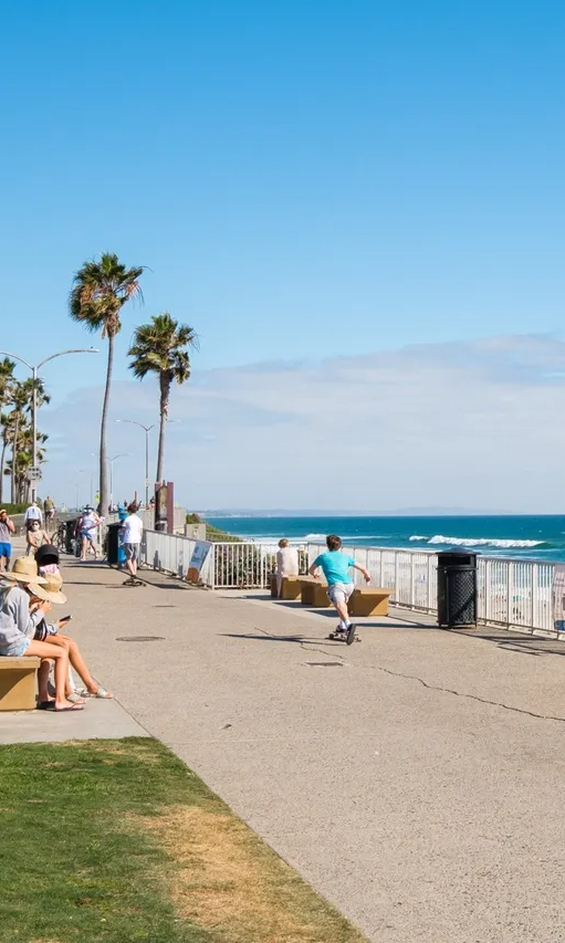 A man is riding a skateboard on a sidewalk next to the ocean.