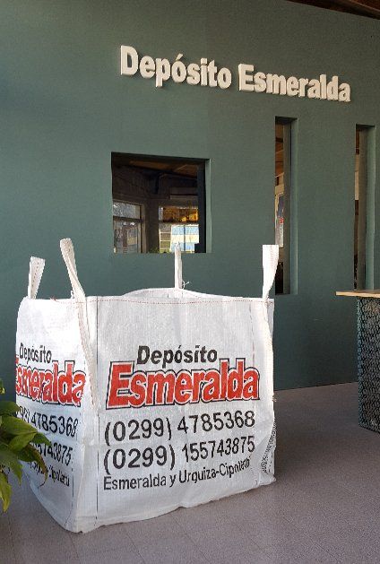 Fachada de Depósito Esmeralda con mesa blanca con el logo de la marca y pared verde en la entrada.