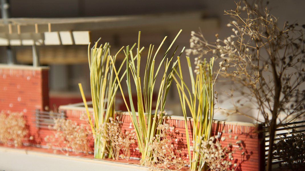 Architectural model with brick wall, tall yellow-green grasses, and a tree with brown leaves.