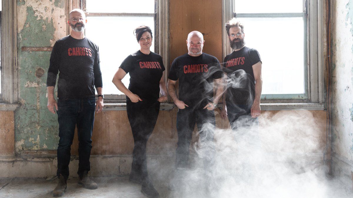 Four people in black shirts, standing by windows with peeling paint, smoke at their feet.